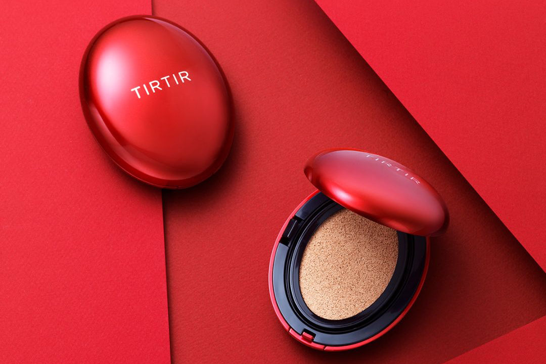 TIRTIR cushion foundation compact in a metallic red case, shown open with the cushion visible, alongside a matching red puff and a closed compact on a red geometric background.